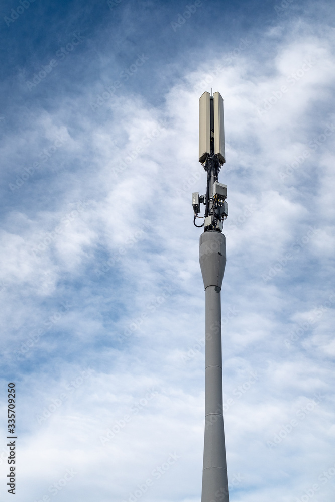 Modern cell phone tower against a blue sky with white clouds.