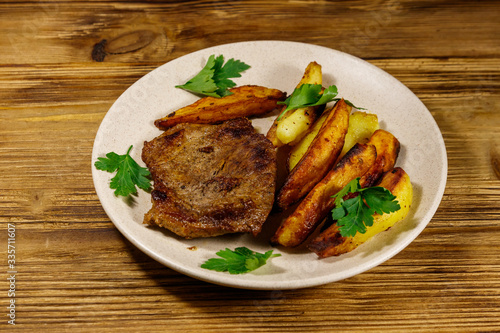 Fried beef steak with potato wedges on wooden table