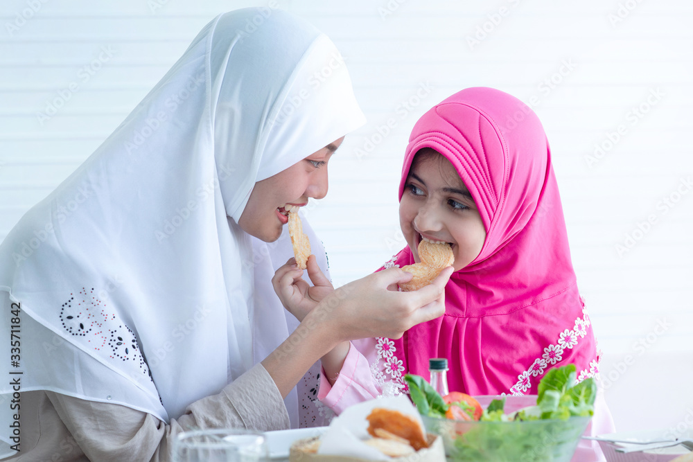 Cute little Muslim girl and mother or older sisters are looking at each other and smiling while eating her cookie Cute little Muslim girl and mother or older sisters are looking at each other and smiling while eating her cookie