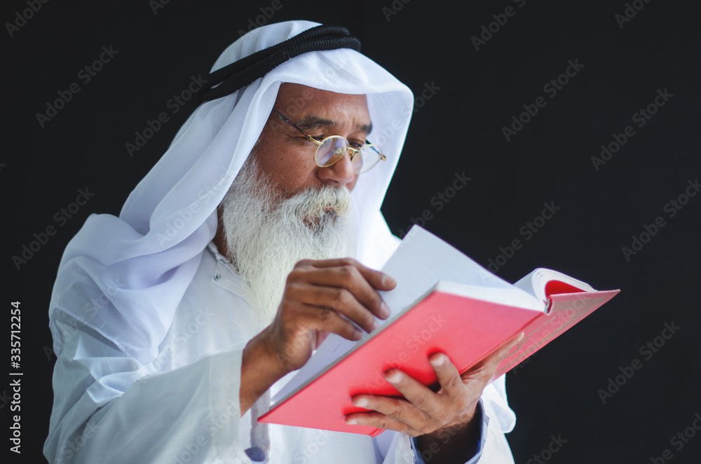 Elderly Muslim Arabic man reading the holy book Quran, black background ...