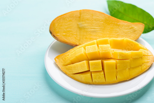 Ripe mango fruit sliced to cubes on white plate and leaf on pastel color background, tropical fruit