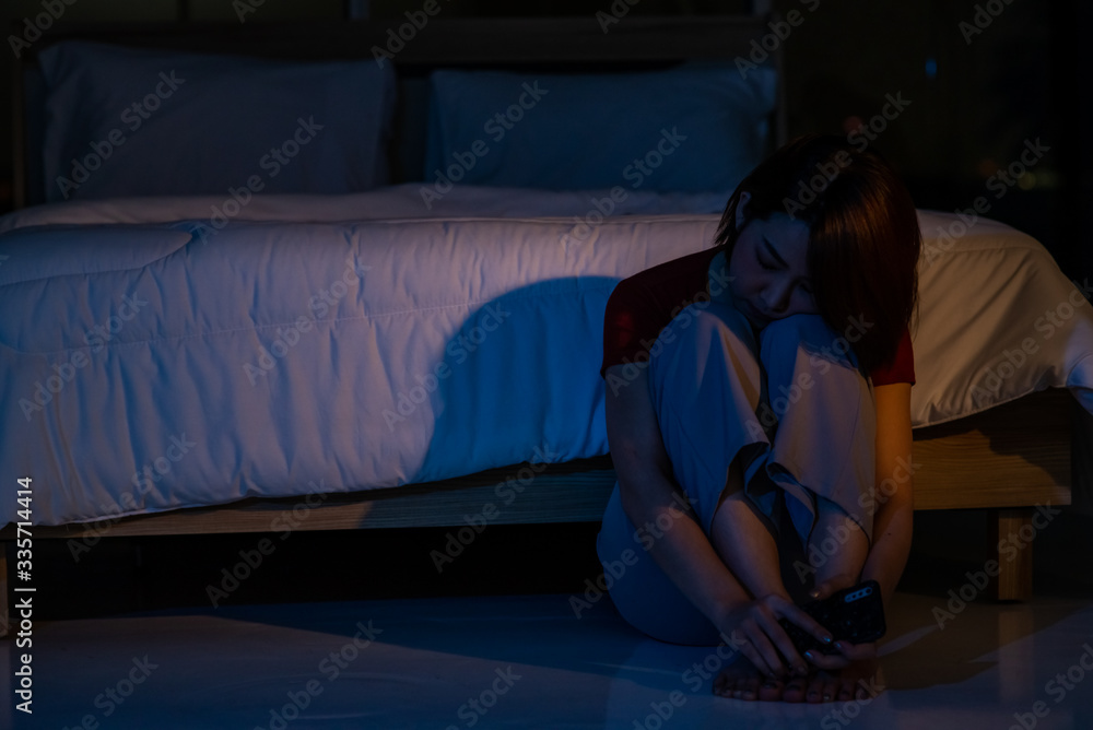 Depressed young beautiful Asian woman sitting alone on bedroom floor with hugging knees at night. Stressed insomnia woman thinking of life problems. Mental health, healthcare and social issue concept