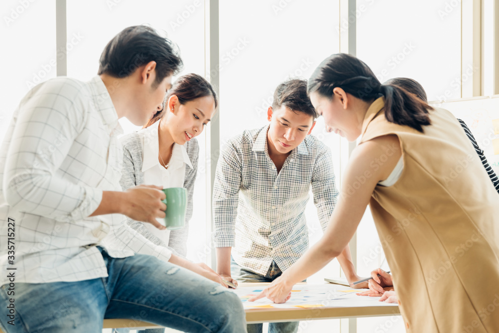 Fototapeta premium Group of asian young modern people in smart casual wear having a brainstorm meeting while sitting in office background. Business meeting, Planning, Strategy, New business development, Startup concept.