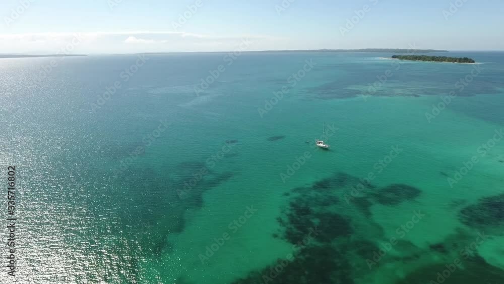 Aerial flight towards a sailboat anchored in the middle of clear aqua colored water with reefs Aerial flight towards a sailboat anchored in the middle of clear aqua colored water with reefs