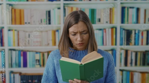 Displeased young woman reading a book gets interrupted by noise can't concentrate distracting showing silent sign at camera in the library. photo