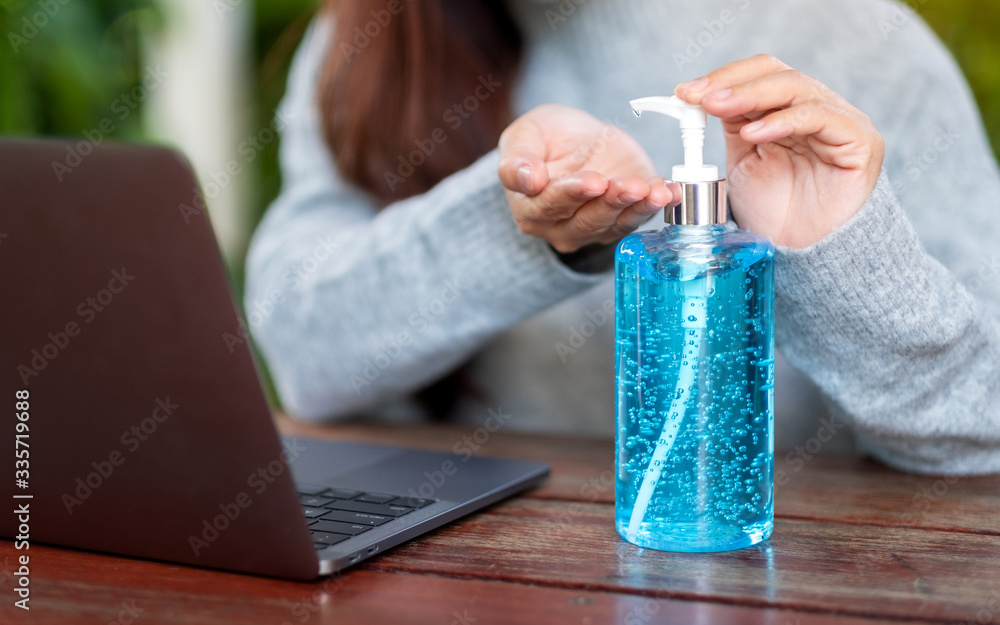 Closeup image of a woman using and applying alcohol gel to clean hands while working on laptop at home for Healthcare and Covid-19 or 2020 virus concept Closeup image of a woman using and applying alcohol gel to clean hands while working on laptop at home for Healthcare and Covid-19 or 2020 virus concept