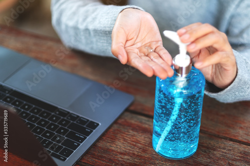 Closeup image of a woman using and applying alcohol gel to clean hands while working on laptop at home for Healthcare and Covid-19 or 2020 virus concept