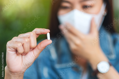 Closeup image of a woman wearing protective face mask and holding white medicine capsule in hand for Healthcare and Covid-19 or 2020 virus concept
