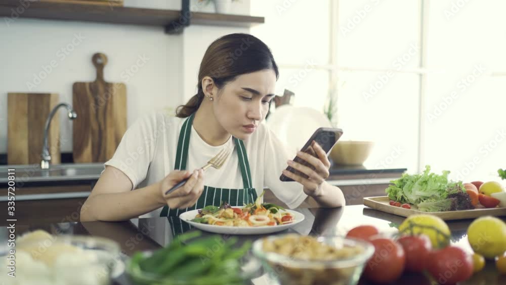 Asian Women Eating Salad While Sitting in Modern Kitchen.And looking at the news with a serious expression.While in the house to be detained during an epidemic Coronavirus(Covid-19).4K Solution. Asian Women Eating Salad While Sitting in Modern Kitchen.And looking at the news with a serious expression.While in the house to be detained during an epidemic Coronavirus(Covid-19).4K Solution.