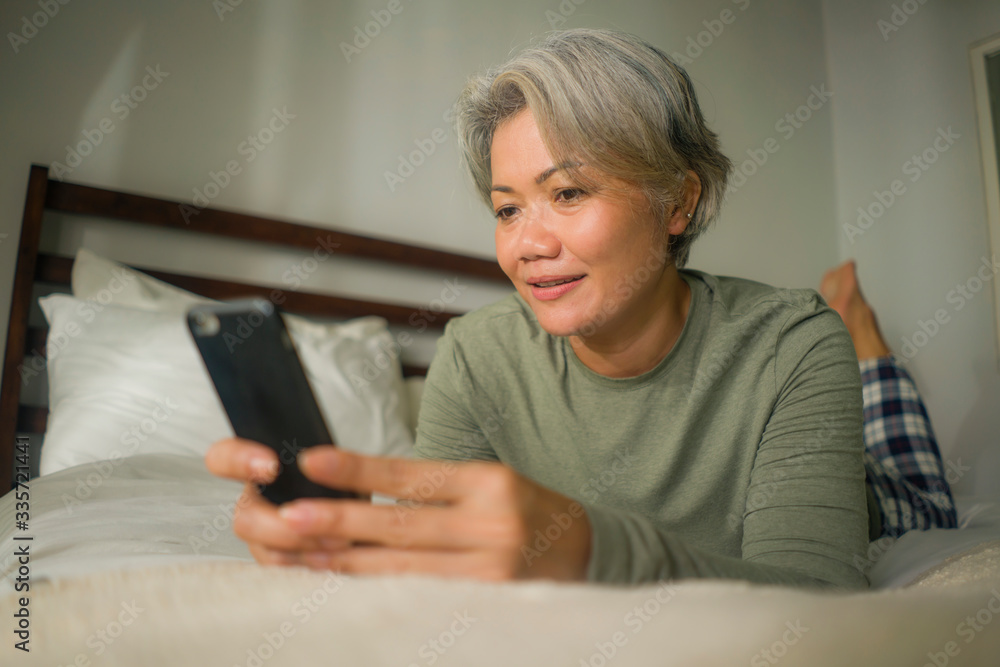 attractive and happy middle aged woman on her 50s using internet mobile phone in bed relaxed and cheerful online dating or enjoying social media app attractive and happy middle aged woman on her 50s using internet mobile phone in bed relaxed and cheerful online dating or enjoying social media app