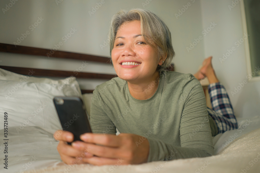 Fototapeta premium attractive and happy middle aged woman on her 50s using internet mobile phone in bed relaxed and cheerful online dating or enjoying social media app