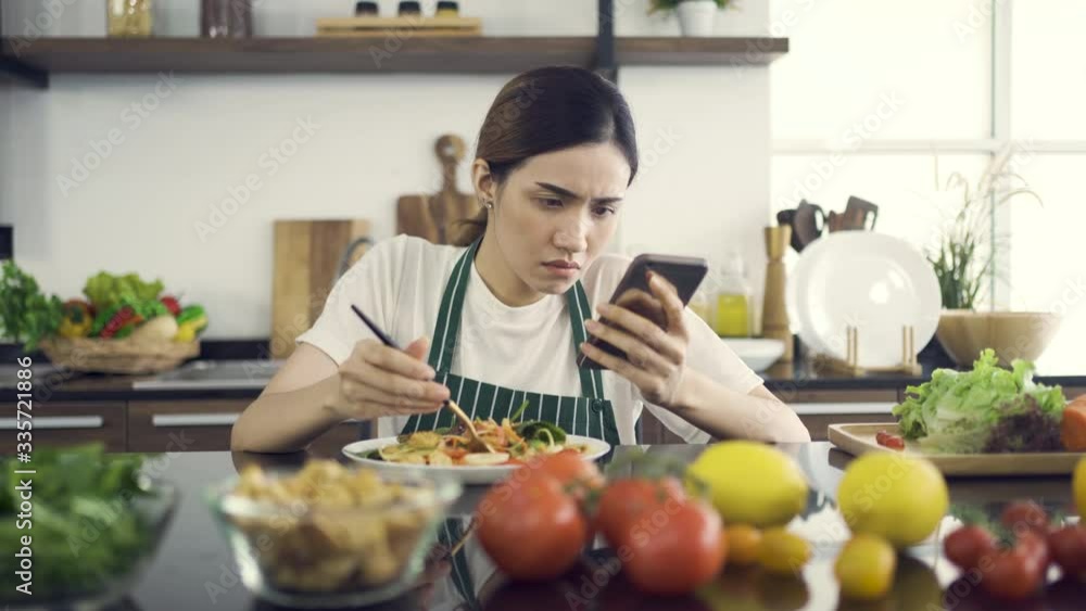 Asian Women Eating Salad While Sitting in Modern Kitchen.And looking at the news with a serious expression.While in the house to be detained during an epidemic Coronavirus(Covid-19).4K Solution. Asian Women Eating Salad While Sitting in Modern Kitchen.And looking at the news with a serious expression.While in the house to be detained during an epidemic Coronavirus(Covid-19).4K Solution.