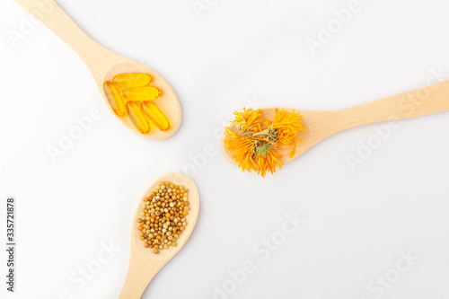 Herbal capsule, natural vitamins, dry calendula flowers at wooden spoon on white background. Concept of healthcare and alternative medicine: homeopathy and naturopathy. Close up, copy space for text
