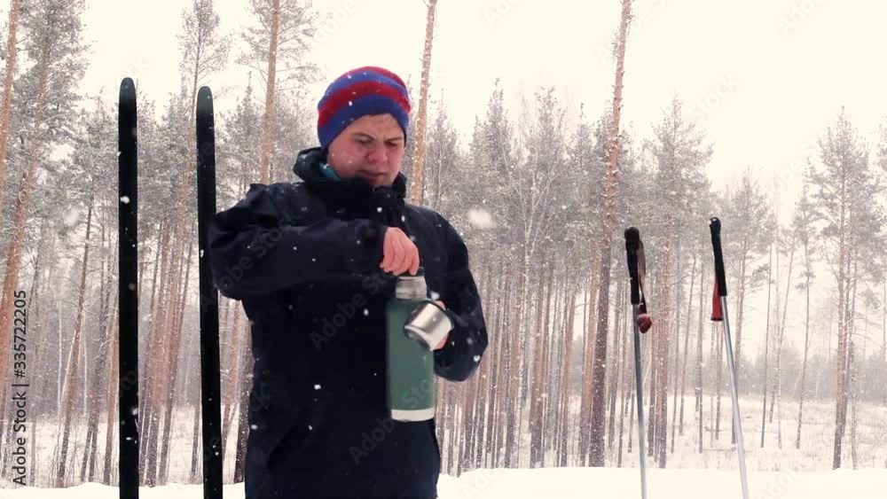 cross-country skier drinks from a thermos at a halt. Winter sports. Active rest in the winter. ski track. young man 20-25 years cross-country skier drinks from a thermos at a halt. Winter sports. Active rest in the winter. ski track. young man 20-25 years
