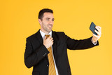 Portrait of confident businessman using smartphone to take selfie on yellow  background.