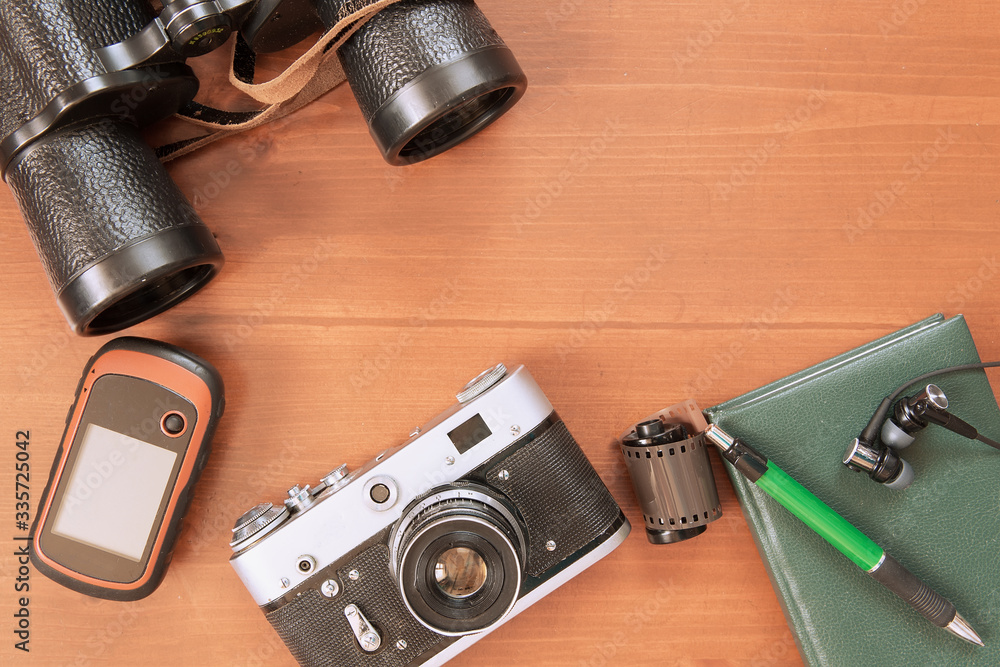 Old camera, reel with photographic film, notebook, binoculars, navigator lie on a wooden background. Travel concept.