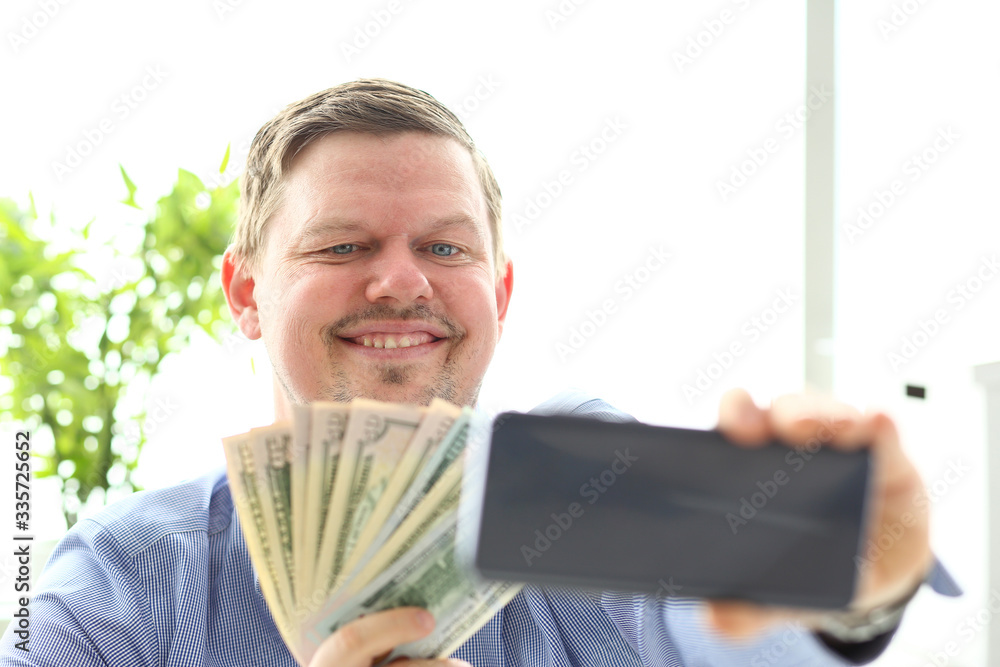 Man making self photo with mobile phone camera posing with pile of US money holding in hands Man making self photo with mobile phone camera posing with pile of US money holding in hands