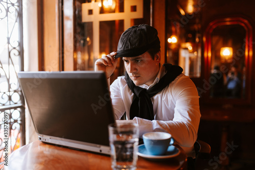  A young caucasian businessman sits in a cafe and works at a computer. Business man working and sitting by window
