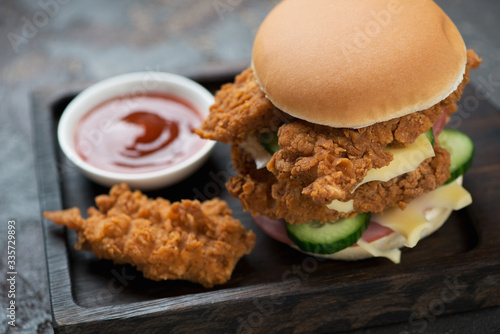 Close-up of a double burger with fried chicken strips on a black wooden serving tray, selective focus