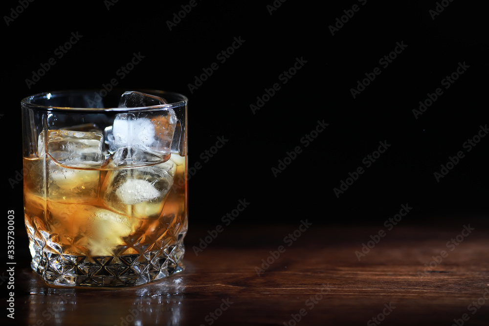 A glass of strong alcoholic drink with ice on a wooden bar counter. Whiskey with ice cubes. Glass with a chilled drink. A glass of strong alcoholic drink with ice on a wooden bar counter. Whiskey with ice cubes. Glass with a chilled drink.