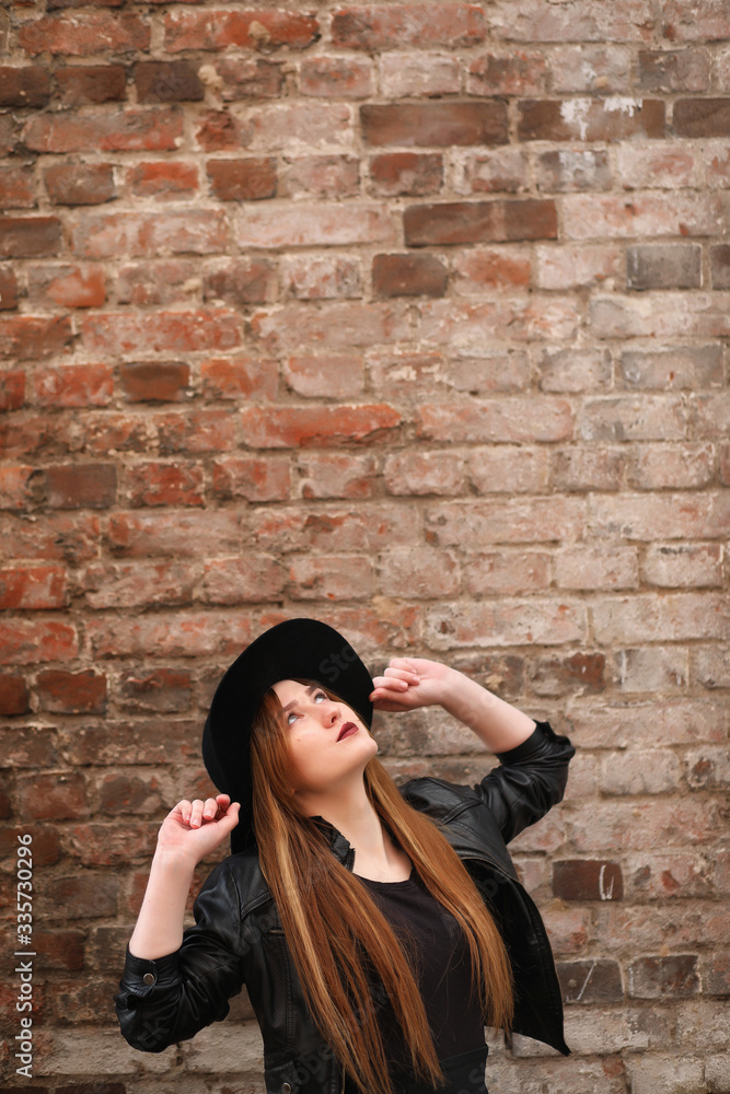 A girl walks down the city street in a leather waistcoat with a phone. Young beautiful girl in a hat and with a dark make-up outside. Girl in the Gothic style on street. A girl walks down the city street in a leather waistcoat with a phone. Young beautiful girl in a hat and with a dark make-up outside. Girl in the Gothic style on street.