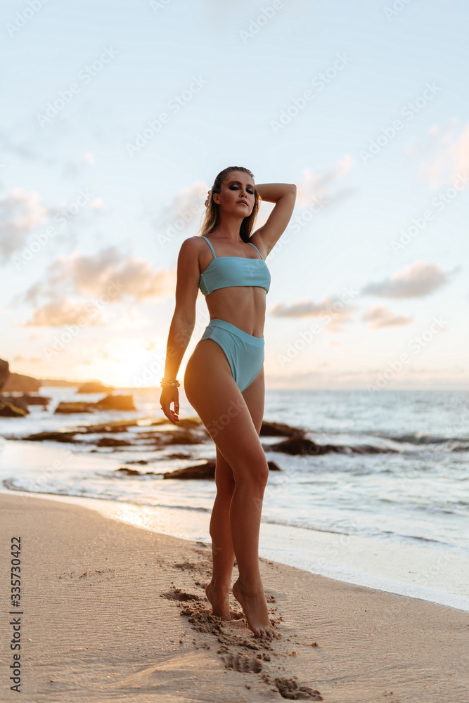 Portrait of attractive blonde girl with long hair posing on beach on sunset background.