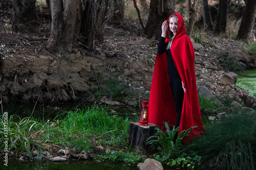 Attractive woman dressed a little red riding-hood cross stream in a dark forest with a lantern