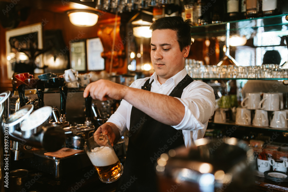 A young caucasian waiter pours beer at a bar