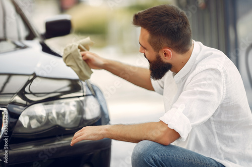 Man in a white shirt. Worker wipes a car. Male holding a rag in his hand