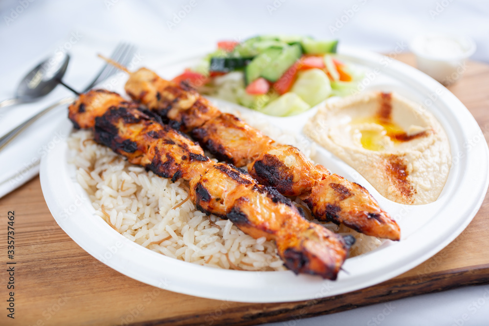 A view of a chicken kabob plate over rice, in a restaurant or kitchen setting.