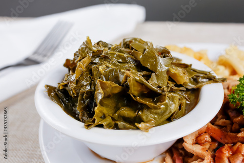 A closeup view of a small bowl of collard greens as a side dish, in a restaurant or kitchen setting.