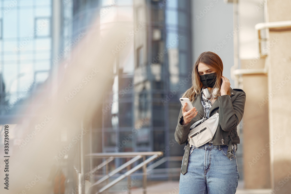 Fototapeta premium Woman in the city. Person in a mask. Coronavirus theme. Girl walks with phone and headphones.