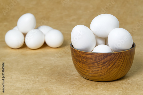 White Eggs isolated in wooden bowl on beige textured background