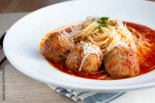 A closeup of a plate of rustic spaghetti and meatballs in a restaurant or kitchen setting.