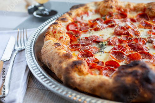 A closeup view of a rustic pizza pie in a restaurant or kitchen setting, featuring toppings as pepperoni.