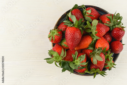 Fresh strawberries in a bowl on white wooden table. Top view. Copy space. Berries background. Beautiful red strawberry. 