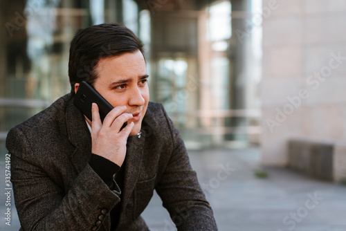  A young businessman sits on a staircase in front of a building with a phone in his hand