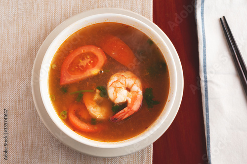 A top down view of a bowl of hot and sour shrimp soup in a restaurant or kitchen setting.