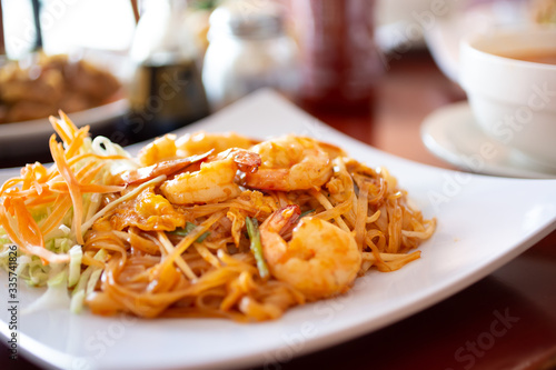 A closeup view of a plate of shrimp pad Thai among several other dishes in a restaurant setting.