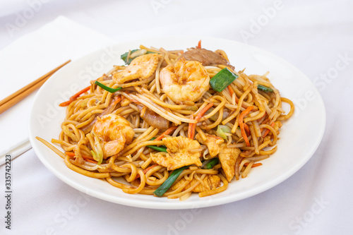 A view of a plate of chow mein, in a restaurant or kitchen setting.