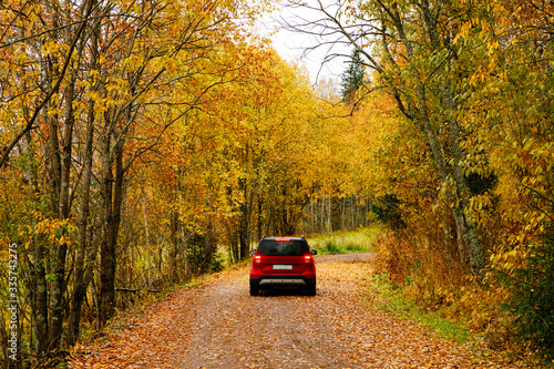 A red car drives along a forest road in autumn. Golden autumn and leaf fall. Concept of traveling by car © dron285