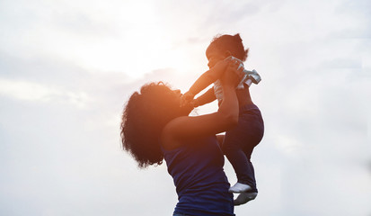 Happy african mother playing with her daughter outdoor on sunny day - Afro mum and child having fun together - Family, happiness and love concept - Focus on faces