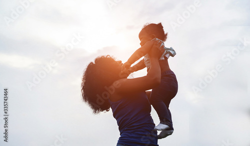Happy african mother playing with her daughter outdoor on sunny day - Afro mum and child having fun together - Family, happiness and love concept - Focus on faces photo