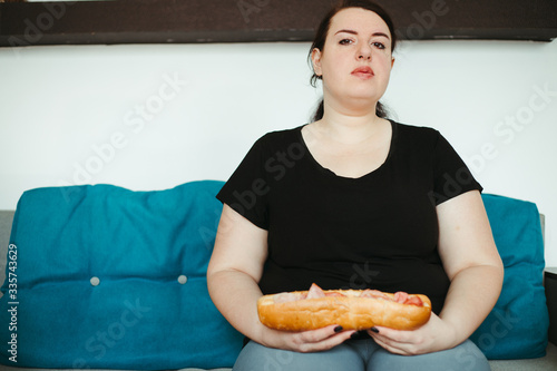 Mindless snacking  home sedentary lifestyle  compulsive overeating. Obese woman sitting on sofa eating unhealthy food