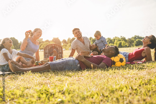 Happy families doing picnic in city park - Young parents having fun with their children in summer time eating and laughing together - Love and chlidood concept - Main focus on left woman face