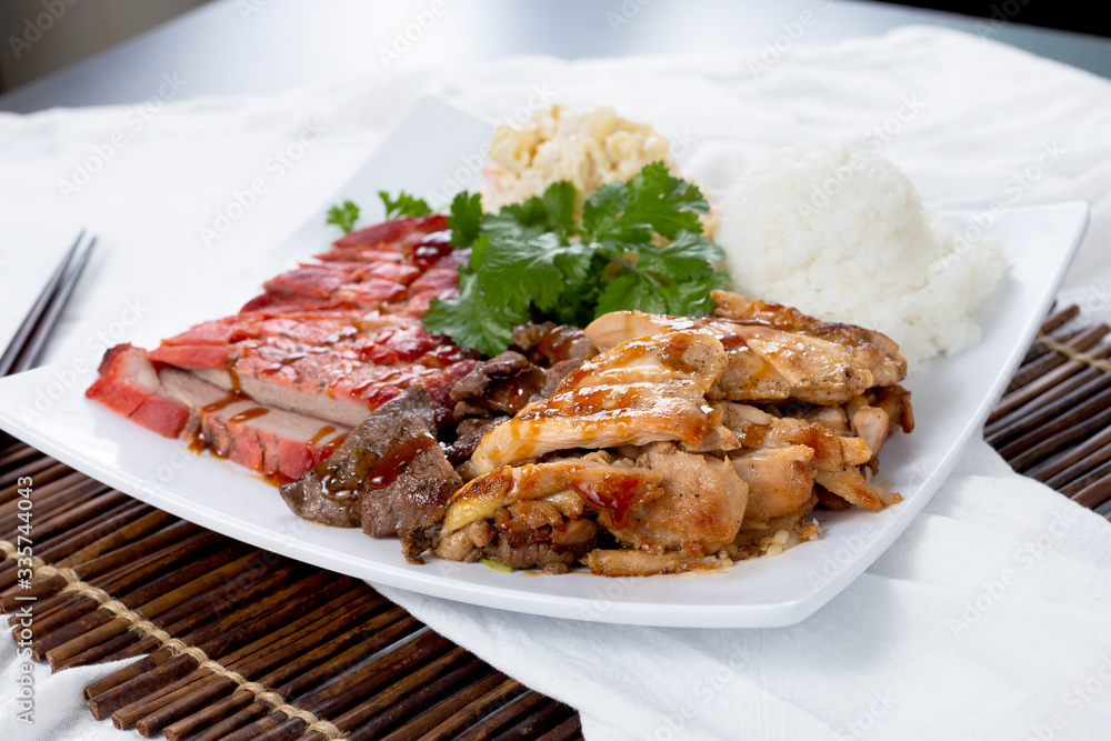 A view of a plate of Hawaiian style barbecue meats and rice, featuring pork, beef and chicken, in a restaurant or kitchen setting.