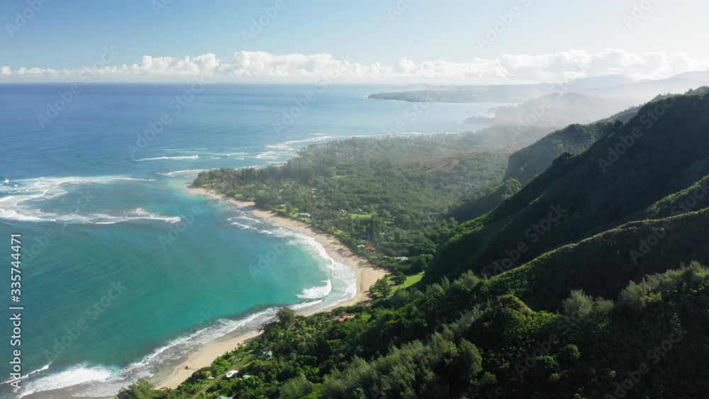 Panoramic aerial view over island coast washed by ocean. Land is covered with tropical green, houses are seen on the shore. Sky is clear with the stripe of white clouds at horizon. Hawaii nature. 4K Panoramic aerial view over island coast washed by ocean. Land is covered with tropical green, houses are seen on the shore. Sky is clear with the stripe of white clouds at horizon. Hawaii nature. 4K