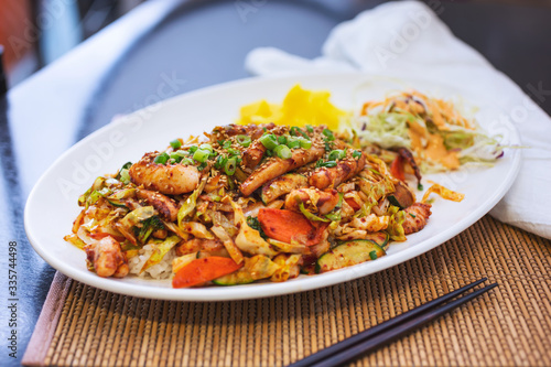 A view of a platter of Korean style spicy squid over rice, in a restaurant or kitchen setting.