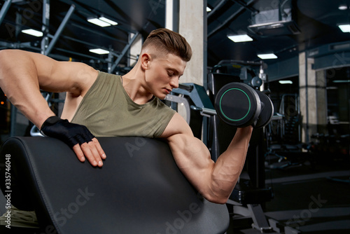 Muscular man building biceps with dumbbell.