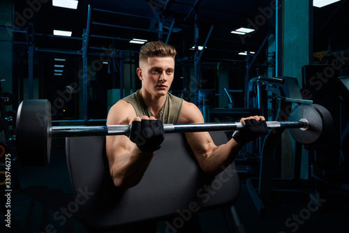 Muscular man training biceps with barbell.